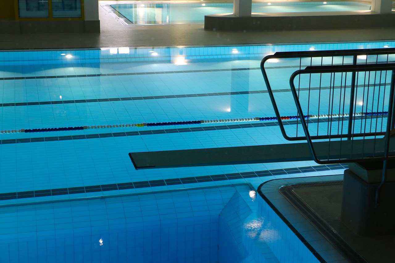 an empty indoor swimming pool at night, a diving board jutting over still blue water