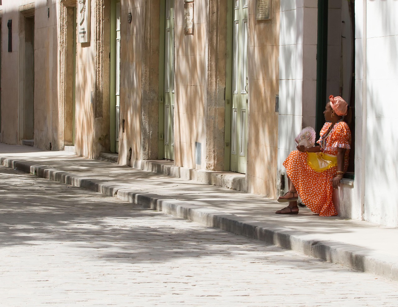 a sun-baked street, with a woman sheltering in a shaded doorway