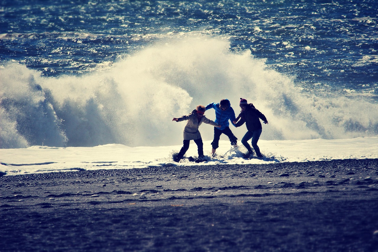 friends on a beach scrambling away from a crashing wave on a wild day