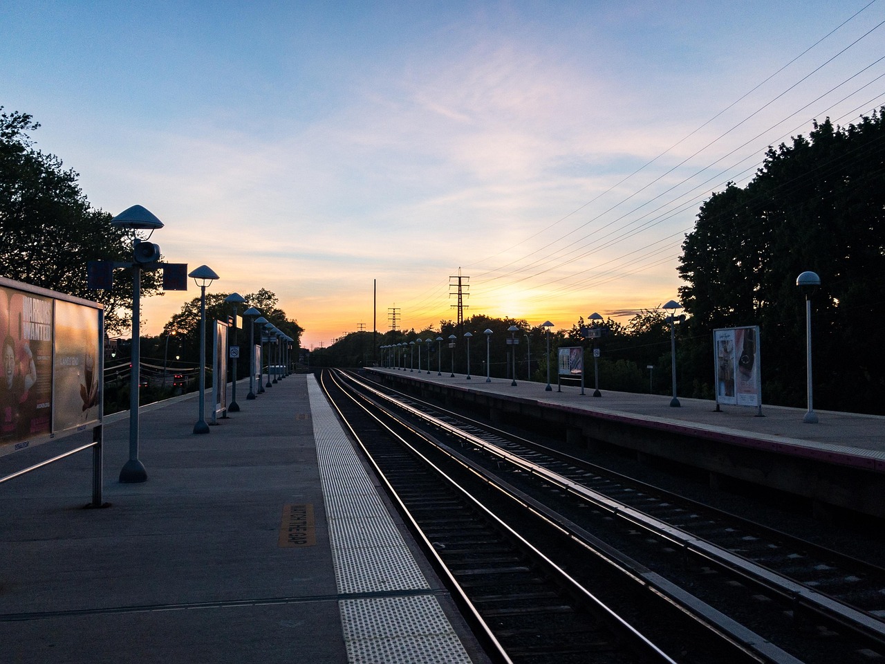 an empty railway platform at dawn, with lamp posts and the sky turning gold