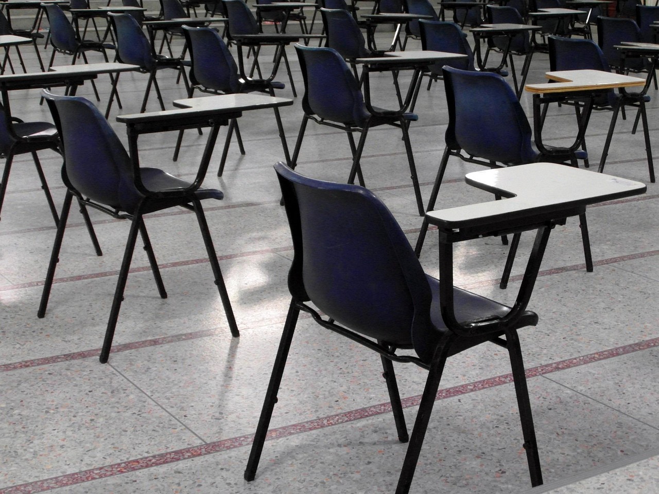 rows of empty plastic chairs with fold-out desks in an exam hall, sunlight on the floor