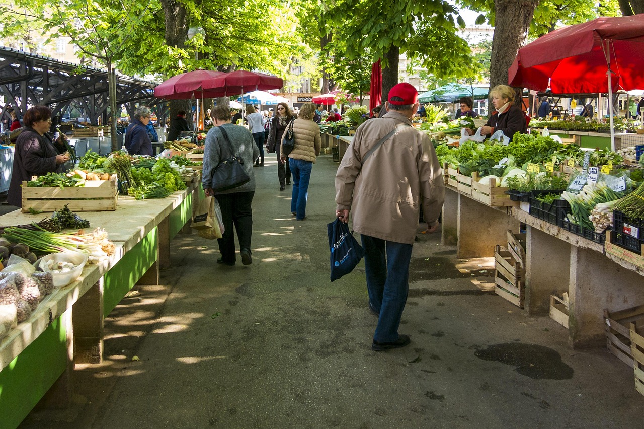a busy outdoor market with traders behind vegetable stalls under red awnings