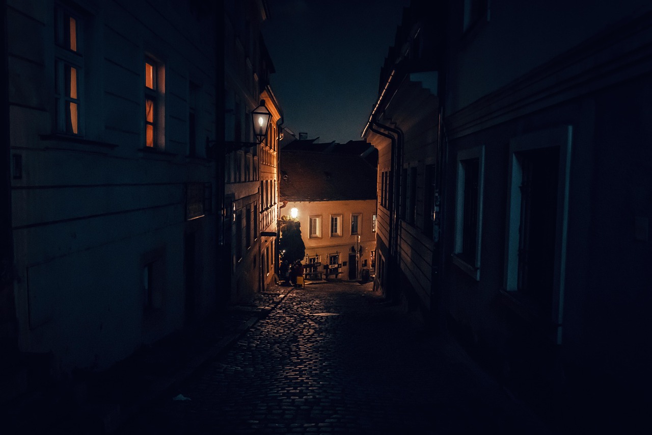 a narrow cobbled lane at night, with a lantern and a few warmly lit windows